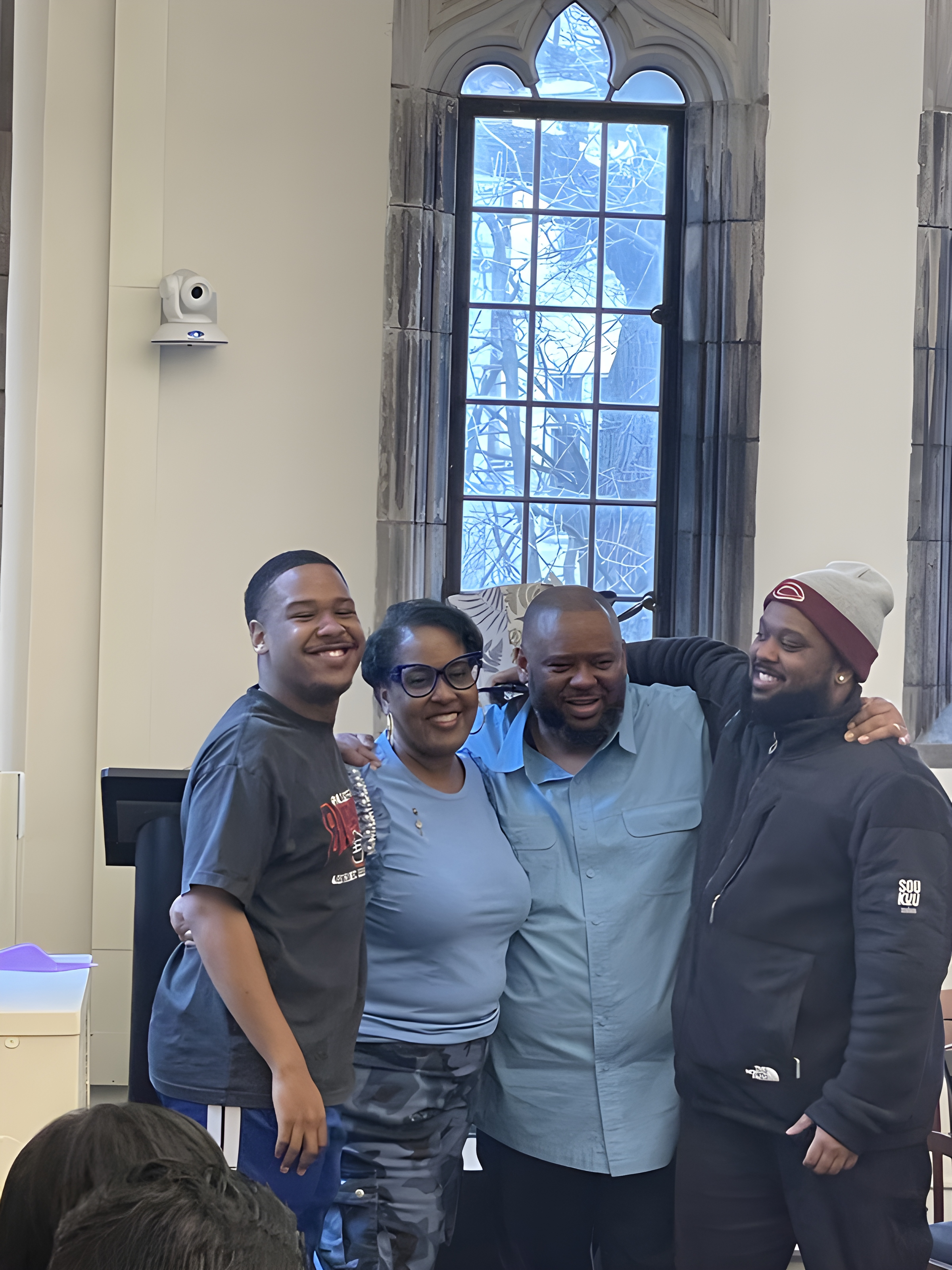 Ashton with family members, arms around each other, smiling together in a church hall