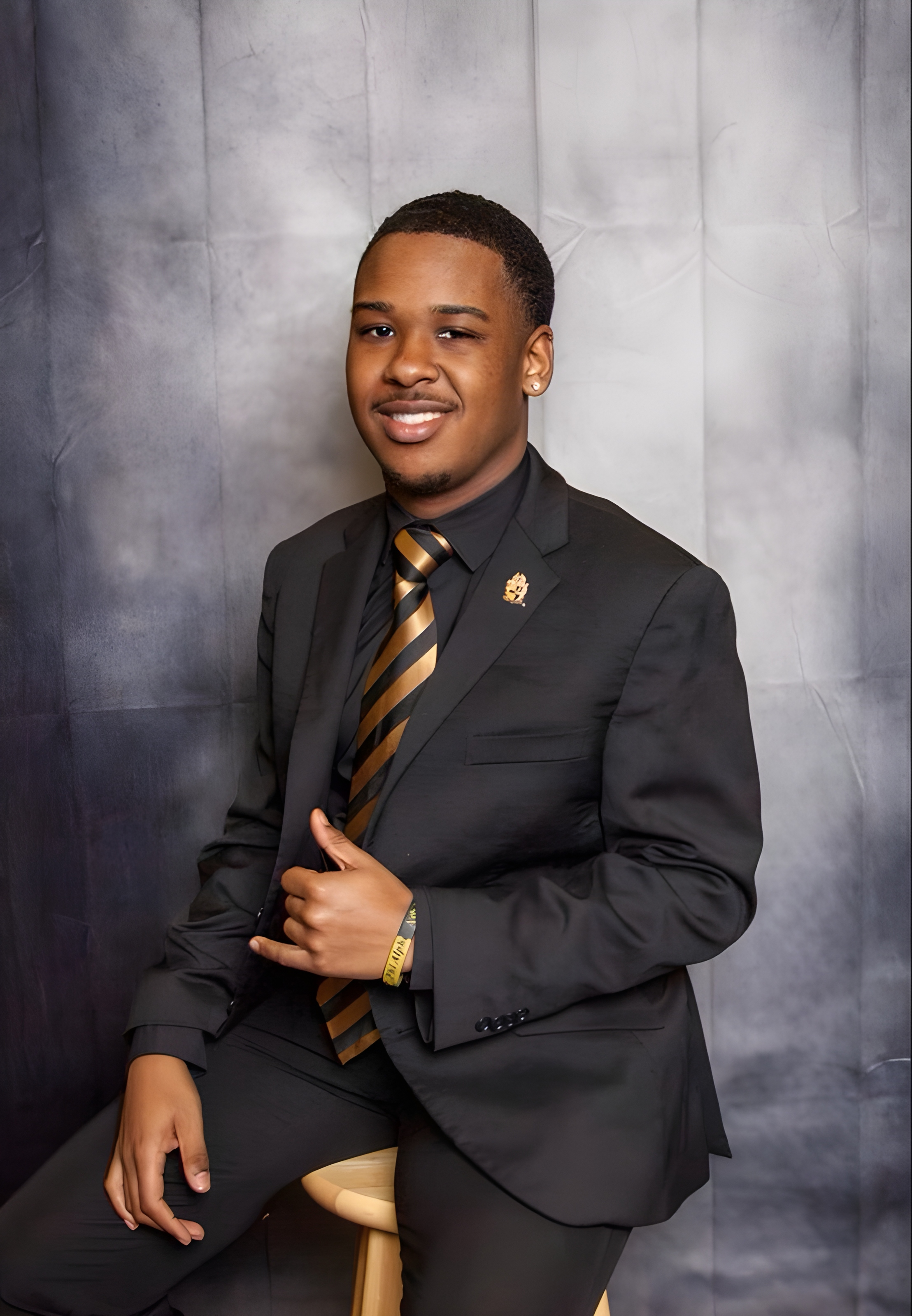 Ashton in a black suit with gold and black striped tie, a formal fraternity portrait
