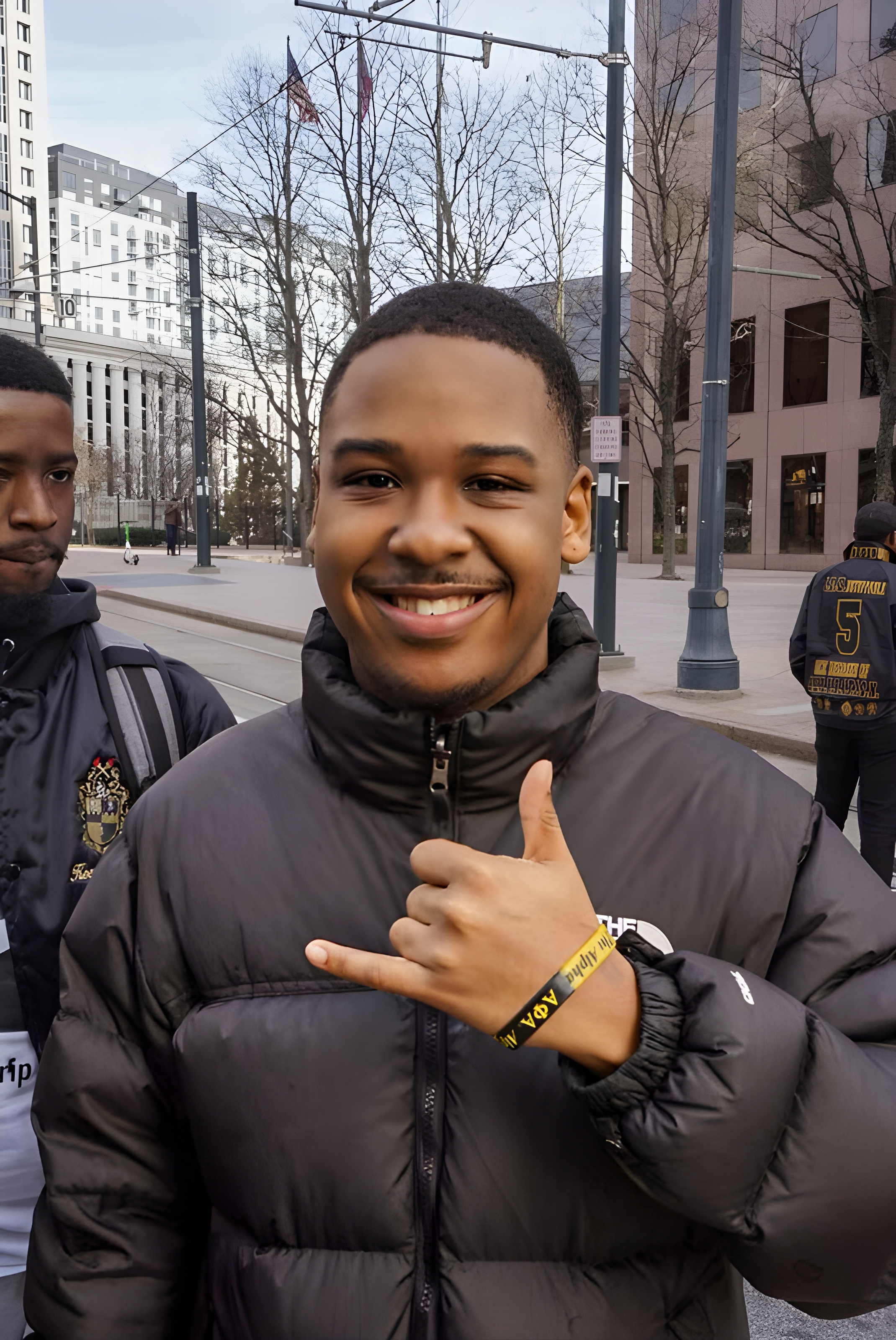Ashton smiling in the city with fraternity brothers, wearing a North Face jacket